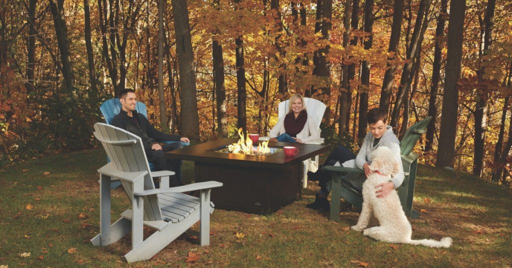 Smiling family sitting around a fire table during Autumn