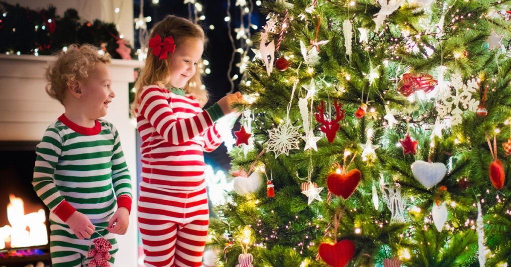 2 toddlers in matching pyjamas while decorating a bright Christmas tree