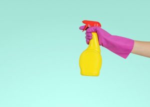 a hand wearing a pink cleaning glove and holding cleaning spray
