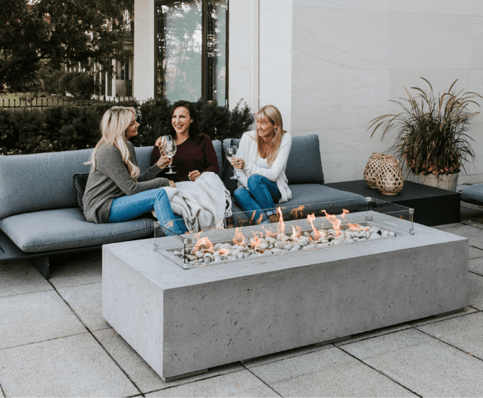3 women sitting around an outdoor fireplace smiling and talking