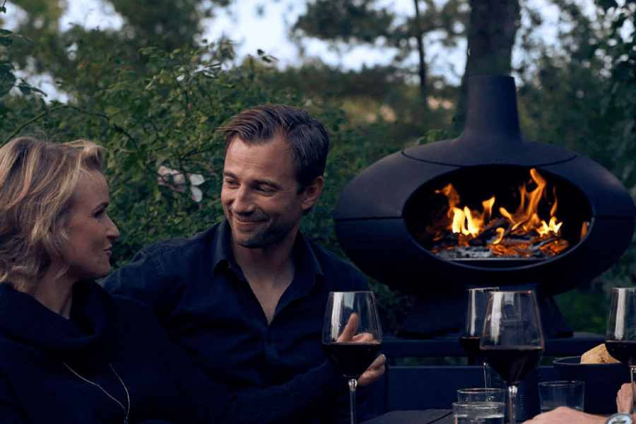 couple entertaining in their backyard next to a wood fire oven