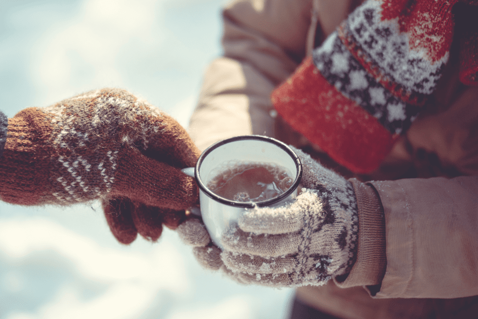 A warm beverage is being passed to gloved hands. 