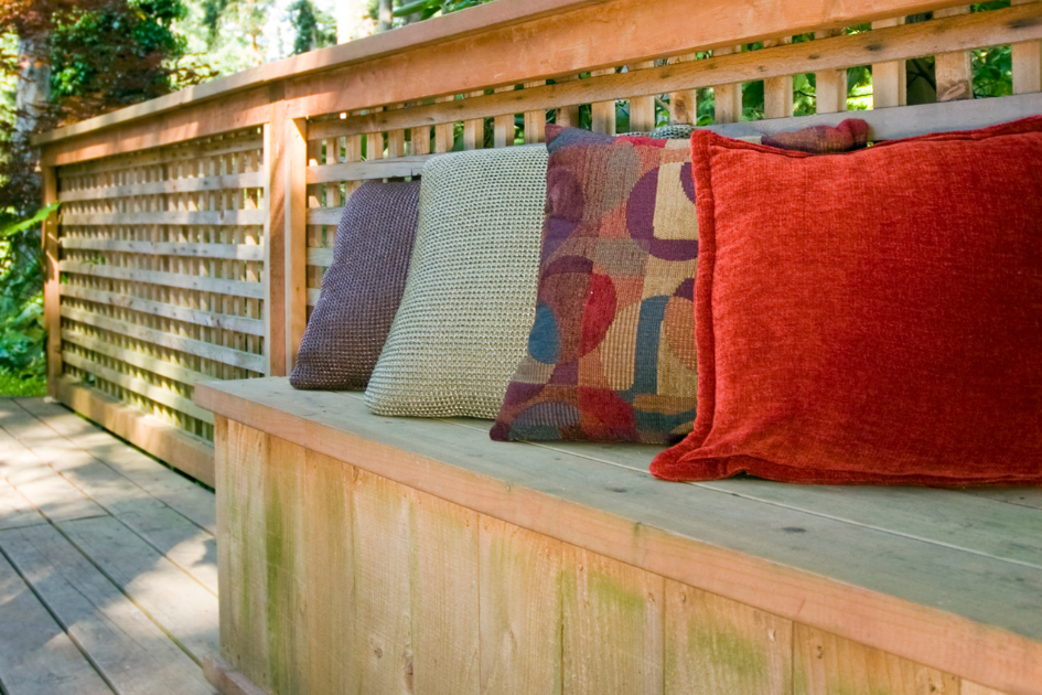 Up close photo of a light coloured wooden patio storage bench with red, purple, yellow and green patterned accent pillows