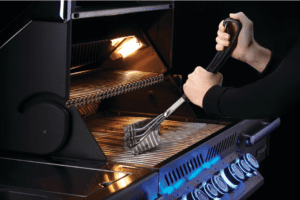 A gas grill being cleaned with a bristle brush