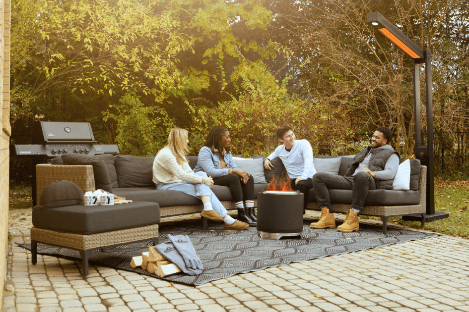 A group of friends are laughing and relaxing around a fire in the backyard.